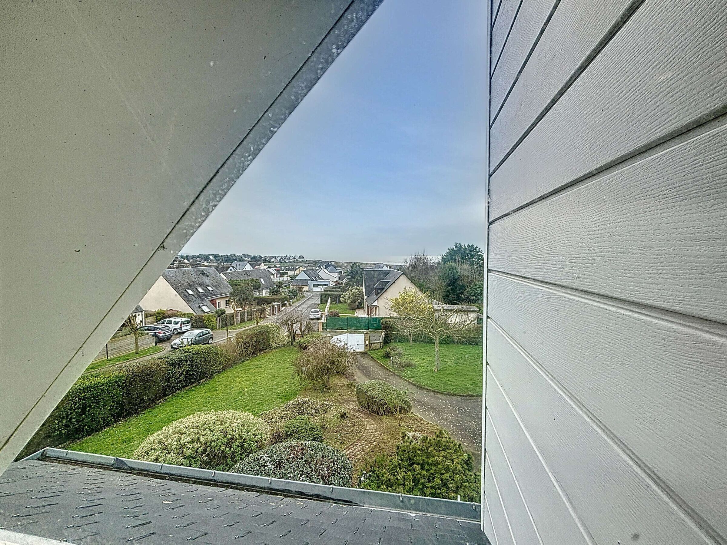 Blick aus einem Fenster auf eine Wohngegend mit Häusern, einer grünen Wiese und einem klaren Himmel.