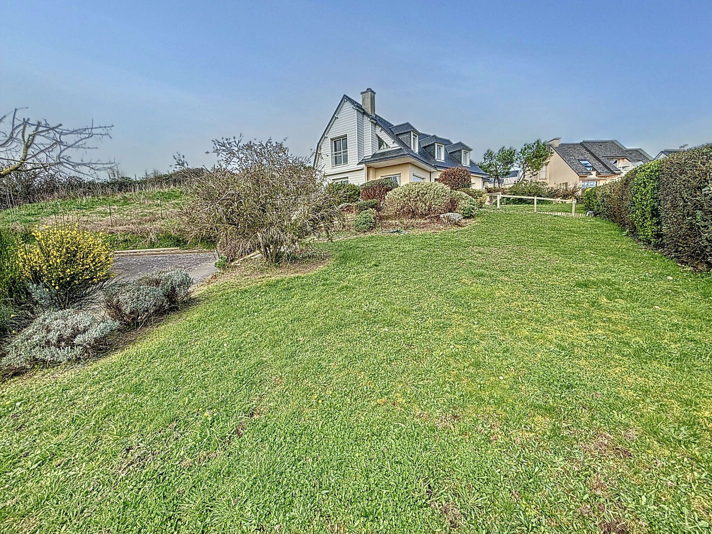 Een woonwijk met een verzorgd gazon, een huis met een puntige dakkapel, en een heldere lucht.