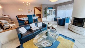 A living room with a sofa, coffee table, and a fireplace. There is a dining area with a table and chairs.