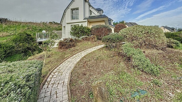 A house with a sloped roof, a chimney, and a paved driveway leading to the entrance.