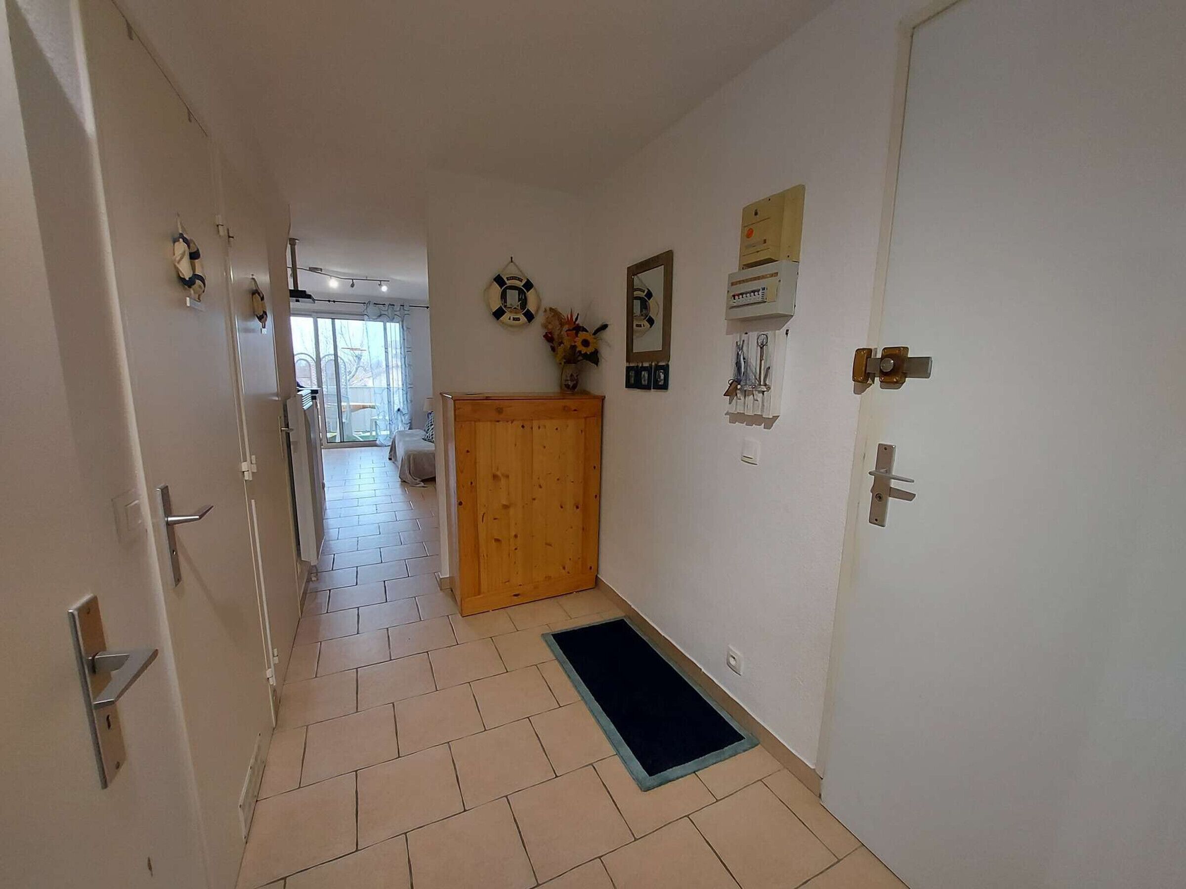A hallway with a wooden door, a blue mat, and a white wall with a clock and a framed picture.