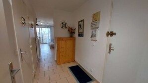 A hallway with a wooden door, a blue mat, and a white wall with a clock and a framed picture. - Beachside 2-BR Apartment for 5 with Private Parking & Terrace in Marseillan (Marseillan-Plage)