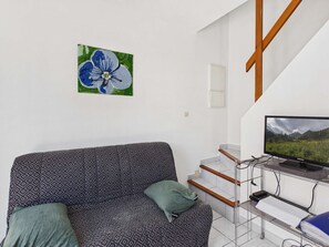 Una sala de estar con un sofá, un cuadro, un televisor y una escalera.