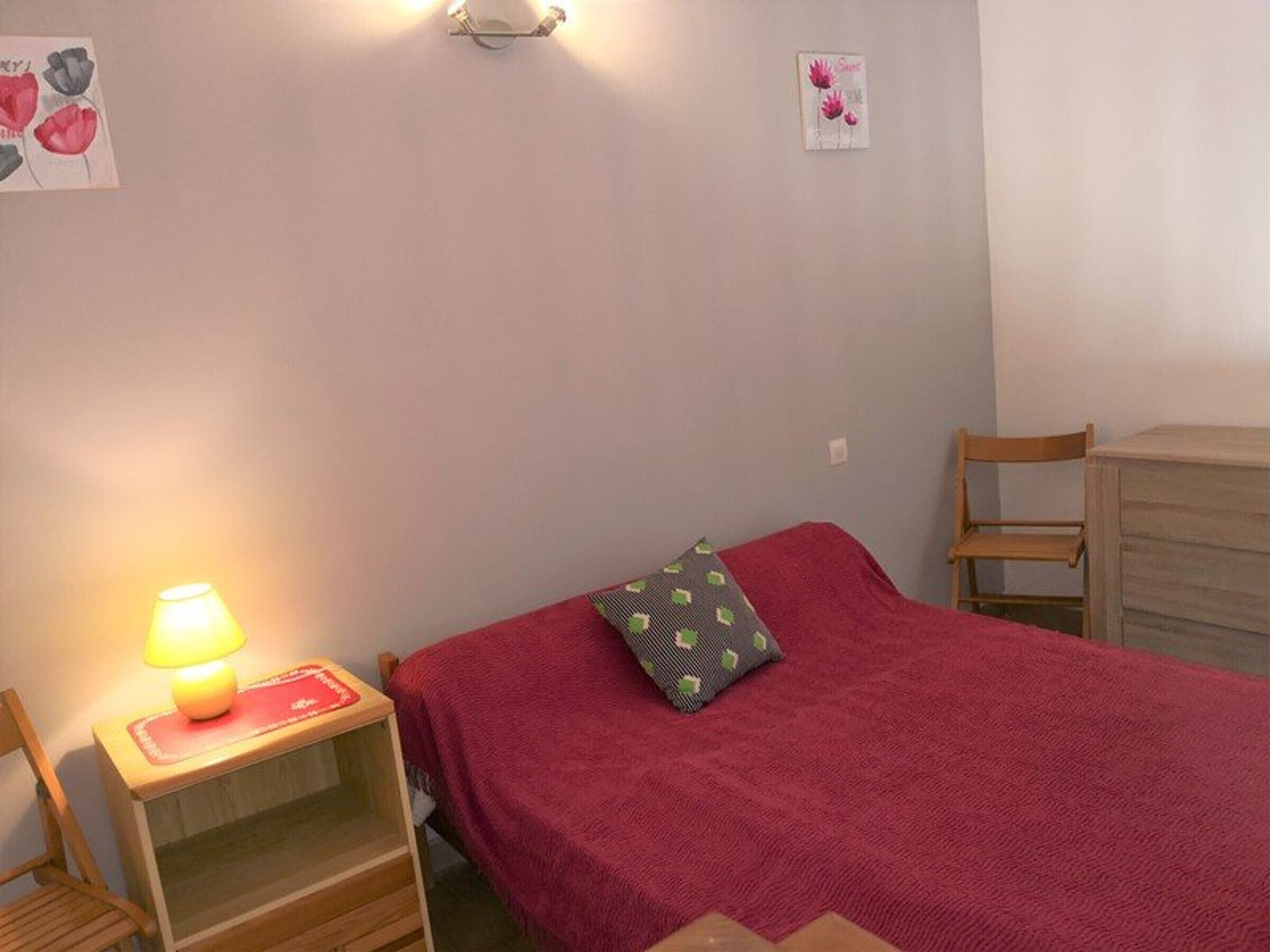 Une petite chambre à coucher, bien rangée, avec un lit simple, une table de chevet avec une lampe, une chaise et une commode.