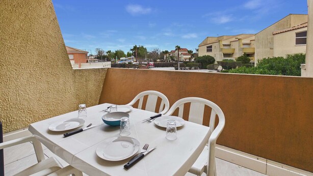 Ein Balkon mit Tisch für zwei Personen, weißen Stühlen und freiem Blick auf die Nachbarschaft.