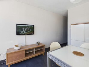 A modern conference room with a wooden console table, a glass table, a white chair, a television mounted on the wall, and a whiteboard.