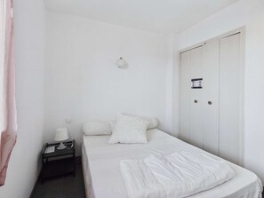 Una habitación pequeña con cama individual, una mesita de noche con lámpara, una puerta con cerradura y una lámpara fijada a la pared.