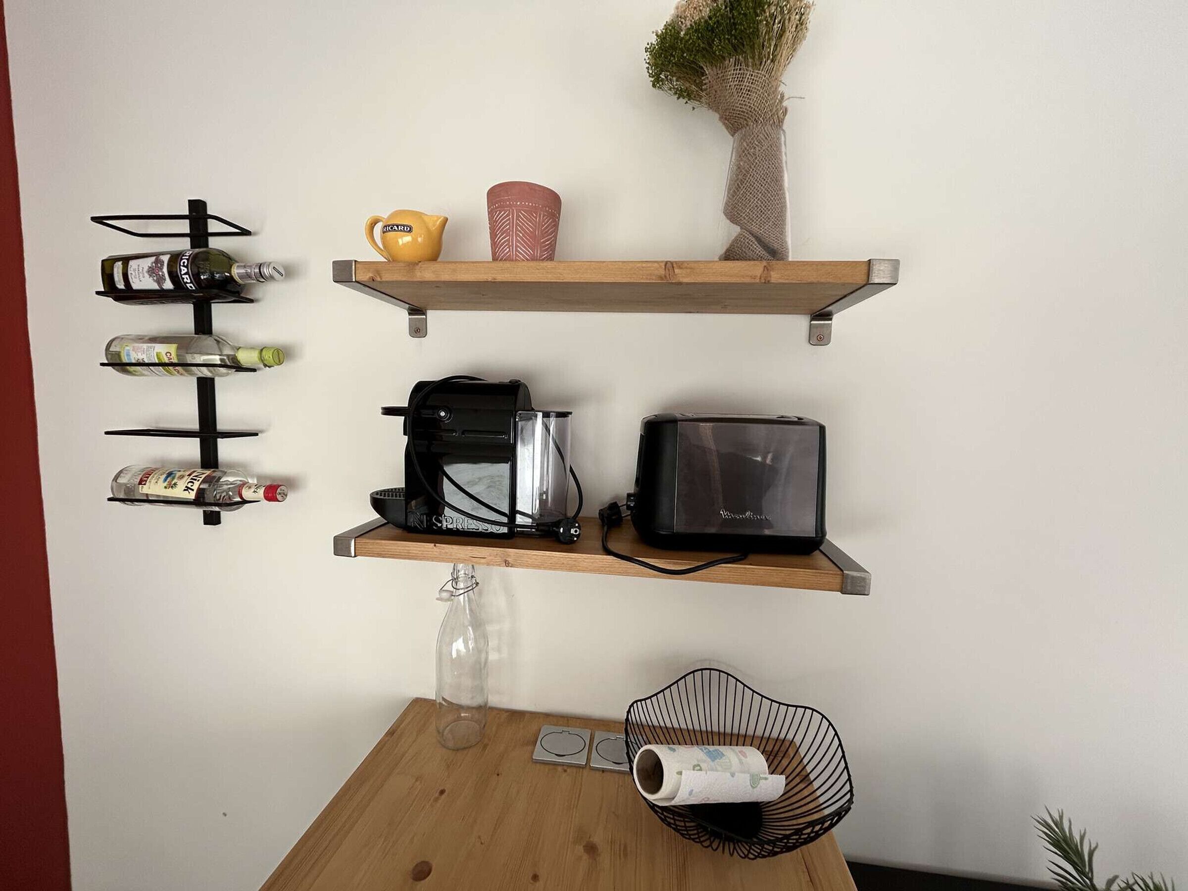 Een keuken met een houten tafel, een koffieapparaat, een broodrooster en een wandrek voor wijn.