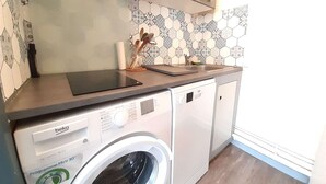 Une cuisine compacte équipée d’un lave-linge, d’un plan de travail et d’un pare-feu en carrelage.