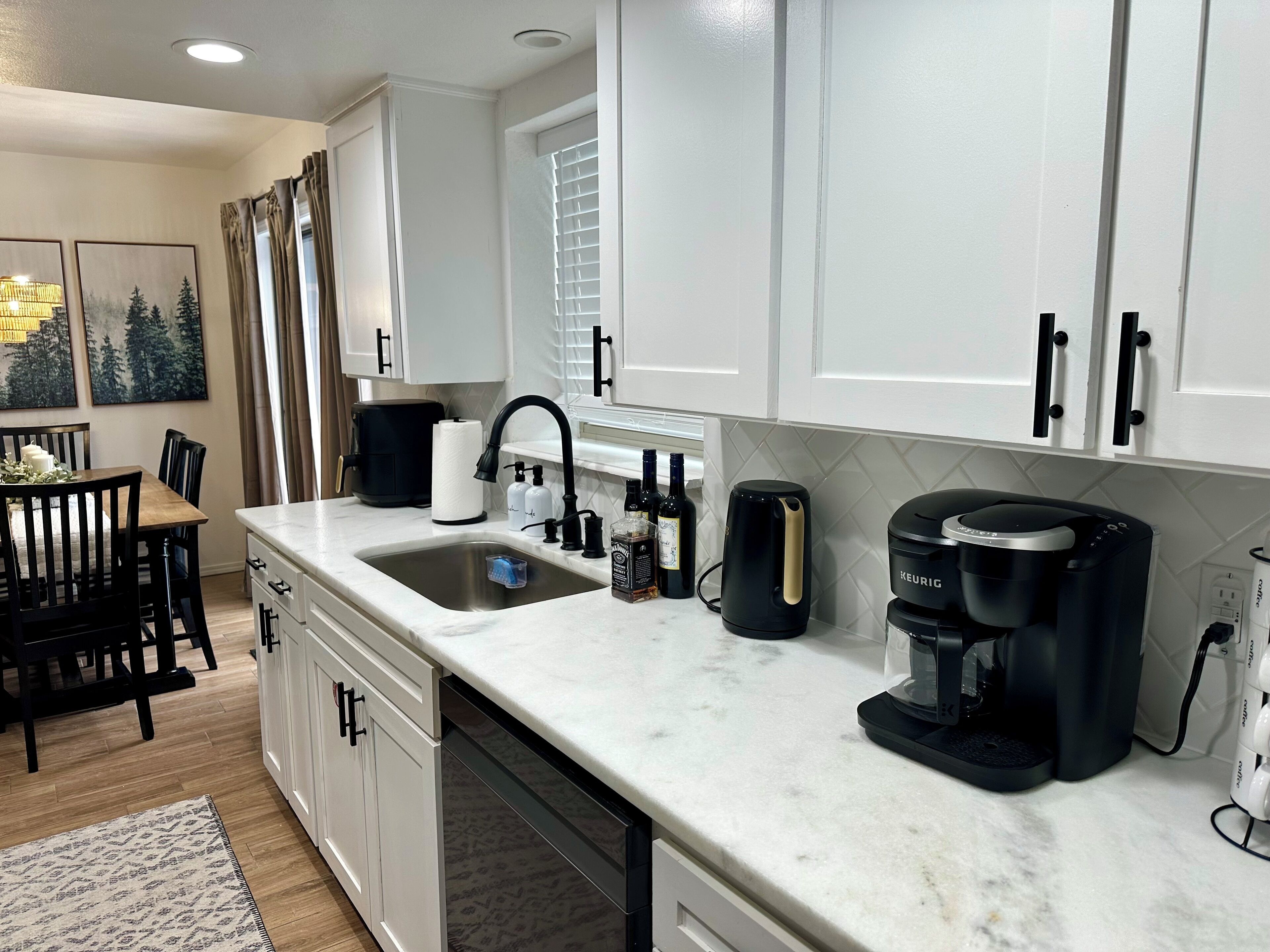 A modern kitchen with white cabinets, a marble countertop, a coffee maker, and a dishwasher.