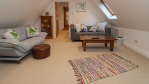 A cozy loft-style living room with a grey sofa, a brown ottoman, a wooden coffee table, and a colorful woven rug. - The Chicken Coop (Shrewsbury)