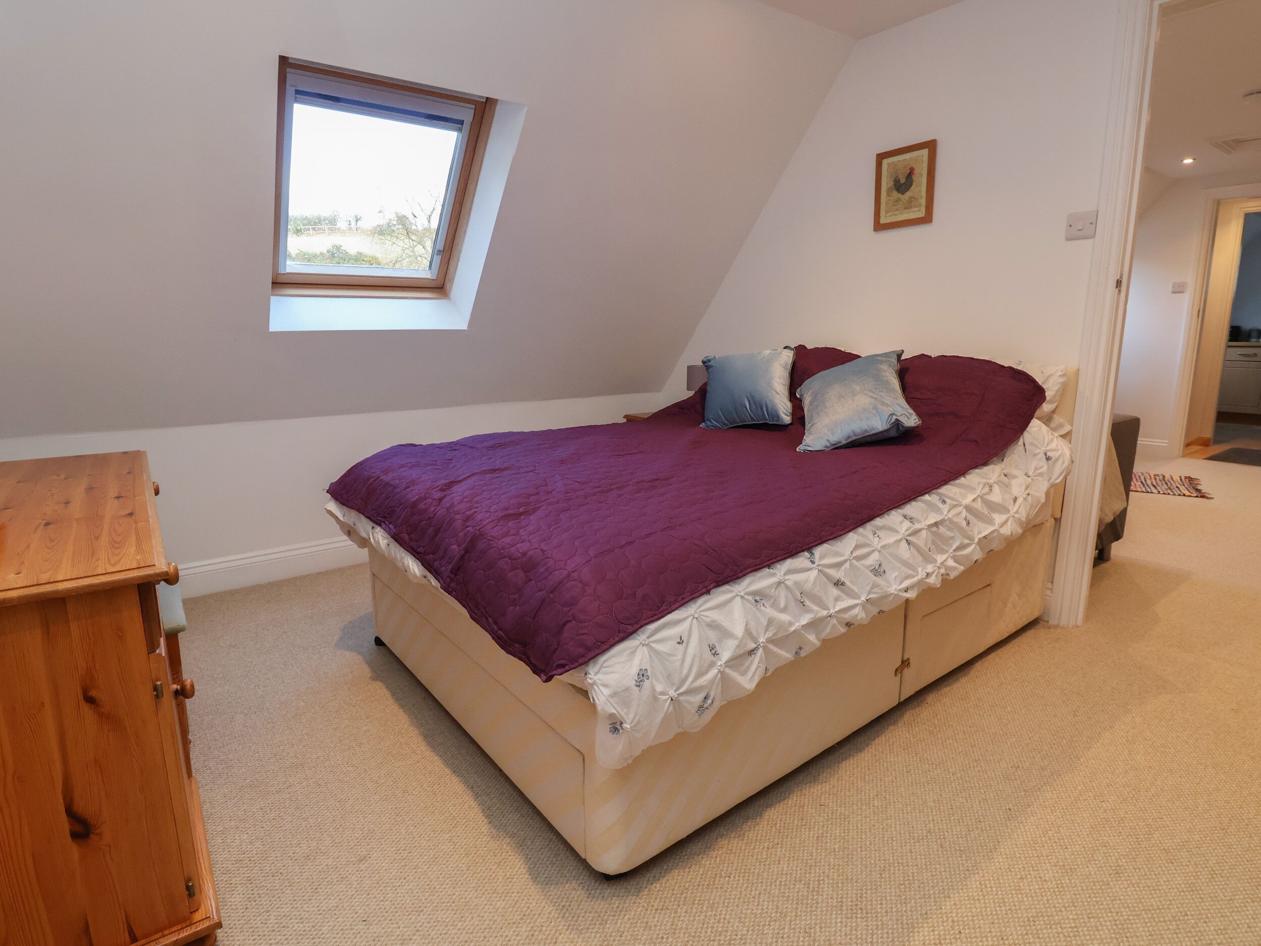 Quarto com cama, mesa de cabeceira de madeira, janela e porta que dá para outro cômodo.