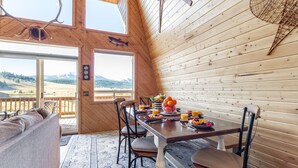 Ein Holzinnenraum mit einem für das Frühstück gedeckten Esstisch, großen Fenstern und Blick ins Freie.