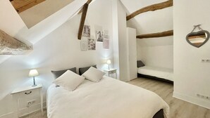 A bedroom with a sloped ceiling, a bed with white bedding, a nightstand with a lamp, and a heart-shaped mirror on the wall. - Chambre Triple Avec Salle de Bains Privative à 10 Minutes de Disneyland Paris (Couilly-Pont-aux-Dames)