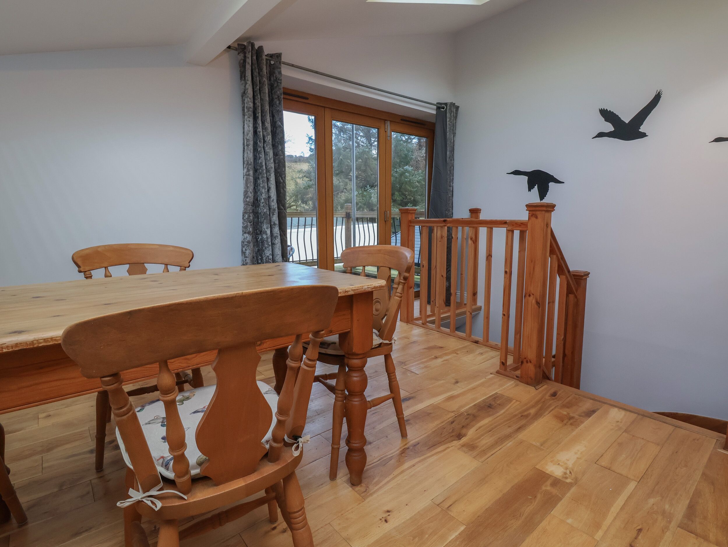A dining area with a wooden table and chairs, a window with curtains, and a wooden railing.