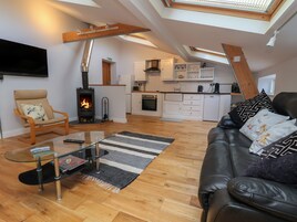 Una sala de estar moderna con una mesa de centro de vidrio, un sofá de cuero, una chimenea y una cocina al fondo.