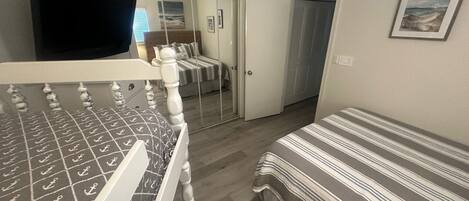 A bedroom with a bed, a TV, a wardrobe, and a door leading to another room.