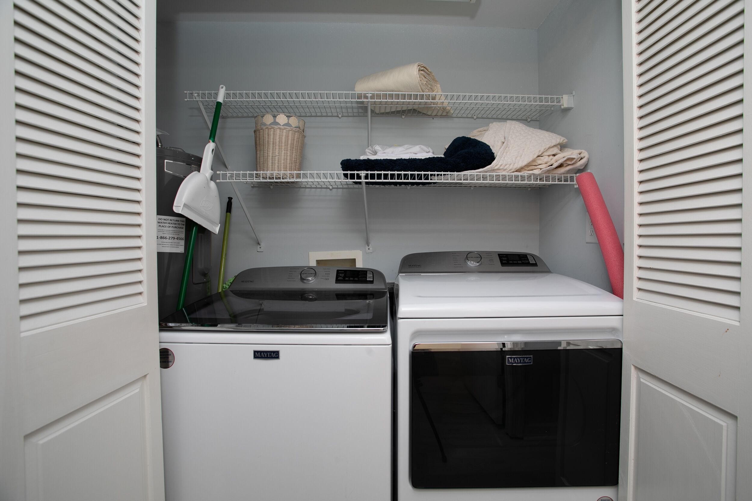 A compact laundry room with a washing machine, dryer, and shelves holding folded towels and a basket.