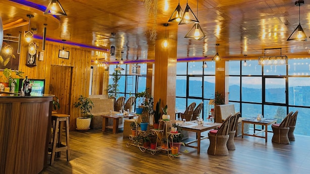 Een gezellig restaurant met houten wanden en plafond, grote ramen met uitzicht op de bergen, en diverse zitmogelijkheden, waaronder tafels en stoelen.
