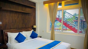 Een hotelkamer met een groot bed, een houten hoofdeinde en een raam met uitzicht op een trap en groen.