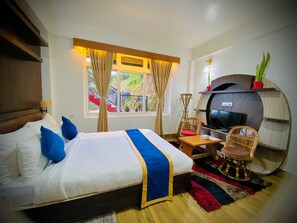 A hotel room with a bed, a television, a seating area with chairs, and a window with curtains.