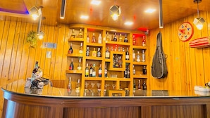 Een bar met houten planken vol diverse flessen en glazen, een toonbank met een QR-code, en een hangende tas.