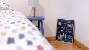 A bedroom with a bed, a bedside table with a lamp, and a poster on the wall.