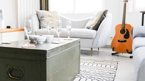 A living room with a grey sofa, a wooden guitar, and a metal coffee table with glasses and bowls.