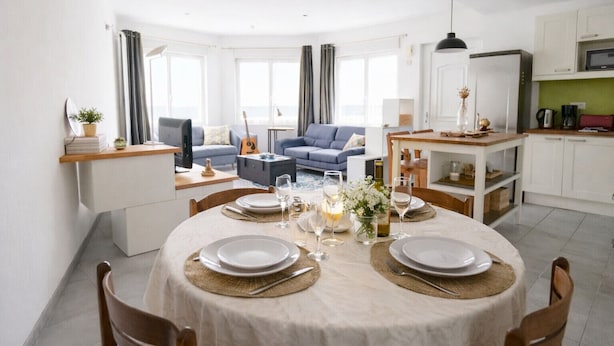 A modern living room with a dining area, featuring a round table set for four, a sofa, and a kitchen area with a microwave and cabinets.
