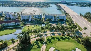 Vista aérea de un campo de golf con una masa de agua, un puente y un complejo hotelero.