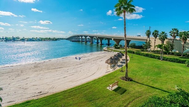 Una playa con un puente, palmeras y un área verde con un banco.