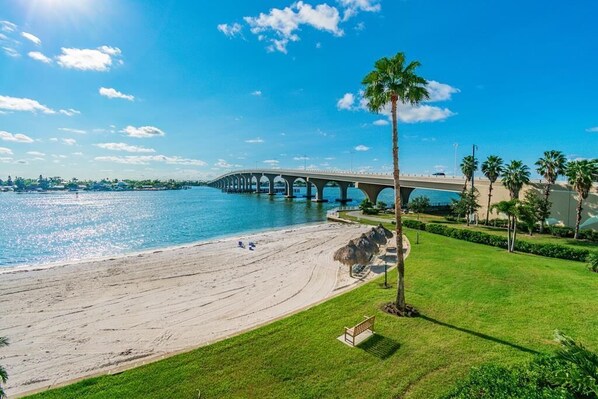 Una playa con un puente, palmeras y un área verde con un banco.