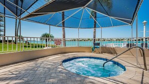 Un área de hidromasaje con vista a la piscina y palmeras, rodeada por un porche cubierto con barandilla.