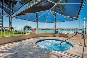 Un área de hidromasaje con vista a la piscina y palmeras, rodeada por un porche cubierto con barandilla.