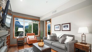A modern living room with a fireplace, a sofa, a coffee table, and a TV mounted on the wall. - Lavish Mountain Condo - Amazing Views! (Canmore)