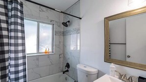 A bathroom with a bathtub, toilet, sink, and a window with a view. - Fillmore Unit 10 | 2BR/1BA (Cape Canaveral)