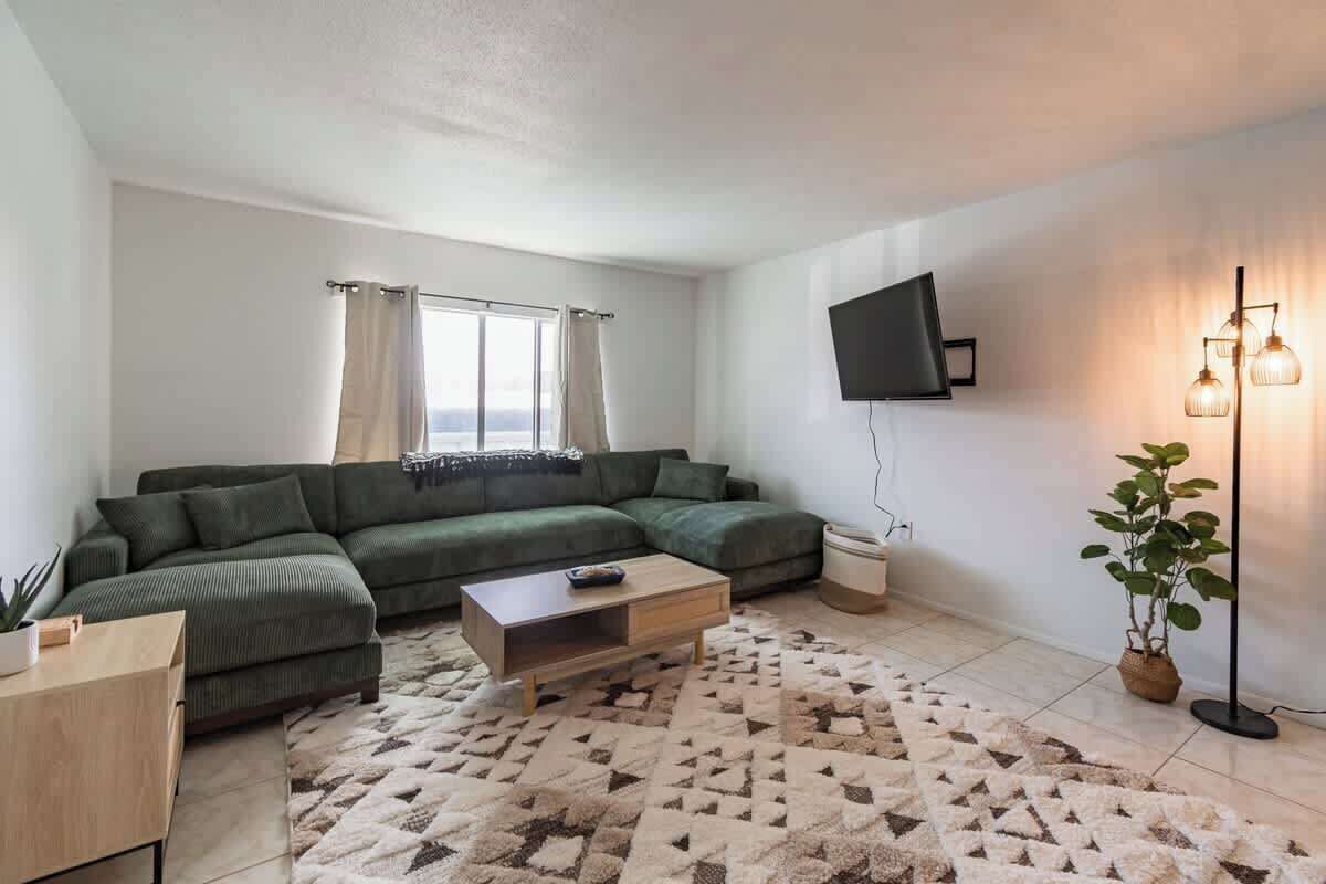 A modern living room with a sectional sofa, a coffee table, a flat-screen TV mounted on the wall, and a floor lamp.