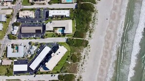 An aerial view of a coastal property with buildings, a parking lot, and a beach. - Fillmore Unit 10 | 2BR/1BA (Cape Canaveral)