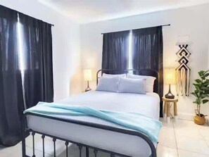 Ett hotellrum med en säng, gardiner, sänglampor och en väggdekoration.