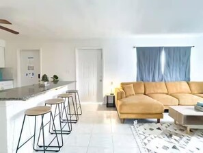Un salon moderne comprenant un canapé, une table basse et un coin bar avec des tabourets.