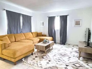 Ein Wohnzimmer mit einer Eckcouch, einem Couchtisch und einem Fernseher.