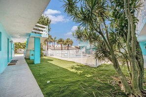 Un couloir d’hôtel donnant sur un espace piscine, avec des palmiers et un ciel dégagé.