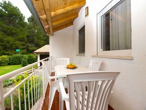 A balcony with white chairs and a table, a window with a curtain, and a view of greenery and a building in the background. - Holiday apartment with air conditioning (Pula)