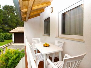 A covered outdoor seating area with a table and chairs, a window, and a door leading to a garage. - Holiday apartment with air conditioning (Pula)