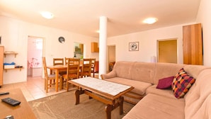 Ett vardagsrum med en beige soffa, ett soffbord i trä och en matplats med ett bord och stolar i trä.