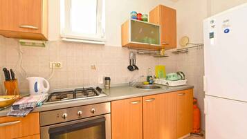 Een koelkast, een oven, een kookplaat, kookgerei, borden en bestek