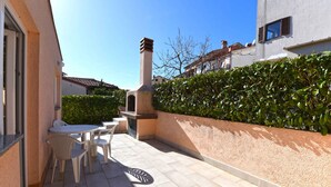A patio with a table and chairs, a small outdoor kitchen, and a wall with a hedge.