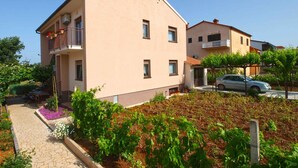 A two-story building with balconies, a paved pathway, and a garden area with various plants. - Holiday apartment with air conditioning (Štinjan)