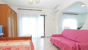 A hotel room with a bed, a pink sofa, a wooden wardrobe, a television, and a bathroom visible through a glass door. - Holiday apartment with air conditioning (Štinjan)