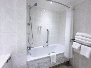A modern bathroom with a freestanding bathtub, a handheld showerhead, and a towel rack with folded towels. - The Aberdeen Dyce Hotel (Aberdeen)